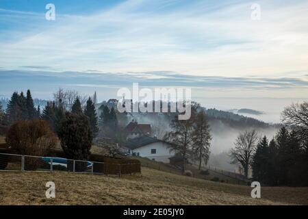 Malerische Drohne Blick auf grünes Tal mit kleinem Dorf von Bäumen umgeben in der Nähe der Bergkette der Alpen in nebligen Morgen. Stockfoto