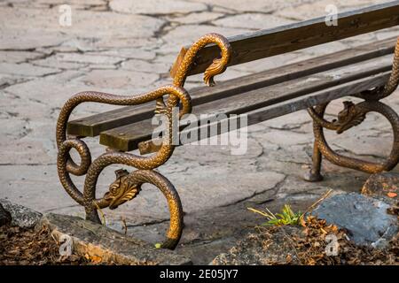 Bank im Park bei Sonnenuntergang mit Metallgeländer in Form einer Schlange oder eines Drachen. Stockfoto