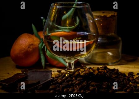 Glas Brandy auf Holztisch mit nahem Schokolade, Kaffee und Mandarinen. Stockfoto