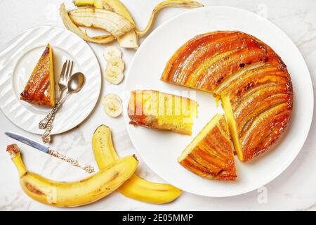 Umgedrehten Bananenkuchen auf einem weißen Teller auf einem Marmortisch, horizontale Ansicht von oben, flach liegend Stockfoto