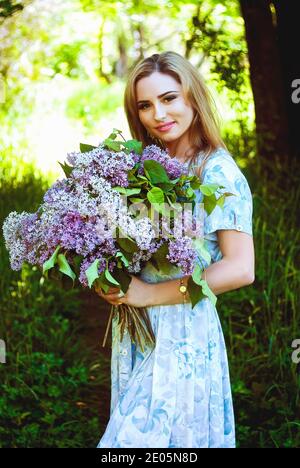 Porträt einer jungen attraktiven Frau im Frühlingsgarten mit einem Strauß Flieder. Federhintergrund. Frauentag. Grußkarte. Stockfoto