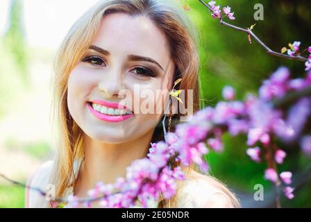 Porträt einer jungen attraktiven Frau im Frühlingsgarten mit blühenden rosa Blüten. Federhintergrund. Frauentag. Grußkarte. Stockfoto