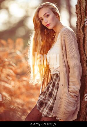 Eine junge natürlich schöne Frau mit langen blonden Haaren trägt eine Strickjacke in einem redaktionellen Mode Bild im Wald mit herbstlichen Orange Farben aufgenommen. Stockfoto