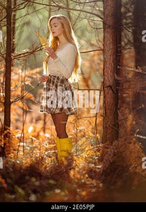 Eine junge, natürlich schöne Frau (20 Jahre) verbindet sich mit der Natur in einem verträumten Bild mit herbstlichen Farben, die von Sonnenschein im New Forest England beleuchtet werden. Stockfoto