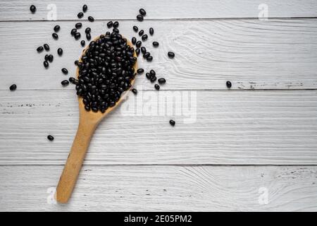 Schwarze Bohnen im Holzlöffel auf weißem Holzhintergrund. Draufsicht. Veganes Lebensmittelkonzept Stockfoto