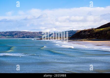 Blick über Benllech Strand bei Sonnenschein mit Schnee auf entfernten Bergen von Snowdonia. Benllech, Isle of Anglesey, Nordwales, Großbritannien Stockfoto