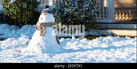 Ein kleiner Schneemann vor der Veranda auf einem Vorgarten in einer Wohngemeinschaft, als die Sonne nach dem Sturm herauskommt. Stockfoto