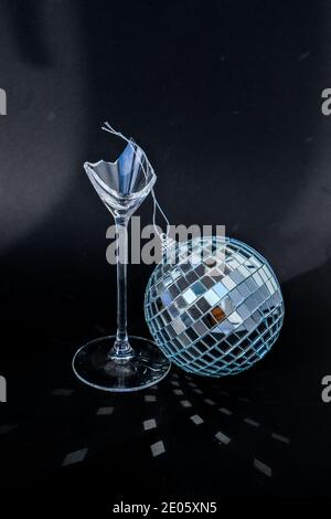 Gebrochenes Champagner-Trinkglas mit Diskokugel. Neujahrsparty, Geburtstag, Mädchentag oder andere Feierlichkeiten. Nach der Party. Kreative Minimal Party Konzept. Schwarzer Hintergrund. Festliches Bokeh Stockfoto