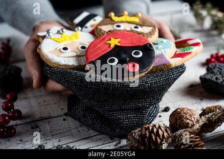Nahaufnahme eines jungen kaukasischen Mannes mit gestrickter Tasche in der Hand mit einem Stapel weihnachtsplätzchen mit verschiedenen Formen und Farben, wie die drei wis Stockfoto