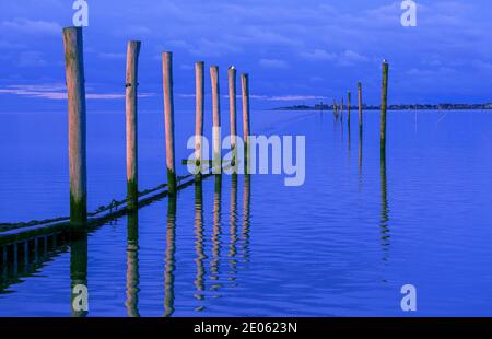 Ein windloser Abend an der Nordsee, Deutschland. Die Holzpfosten führen den Blick über das Wasser auf die kleine ostfriesische Insel Baltrum. Stockfoto