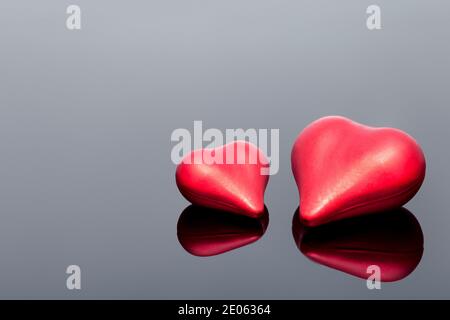 Rote volumetrische Paarherzen das Symbol der Liebe liegt auf schwarzem Glas mit Spiegelung, einsame Herzen mit Kopierraum, niemand. Stockfoto