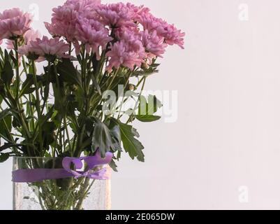 Bouquet von kleinen rosa Chrysanthemen in einer Vase gegen ein Fenster tagsüber Stockfoto