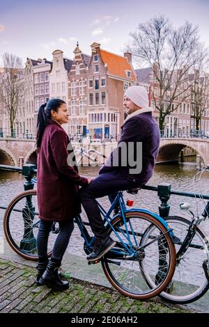 Amsterdam Niederlande bei Sonnenuntergang, historische Kanäle bei Sonnenuntergang. Holländische historische Grachten in Amsterdam, Paar auf Städtereise in Amsterdam, Männer und Frauen am Abend an den Grachten Stockfoto