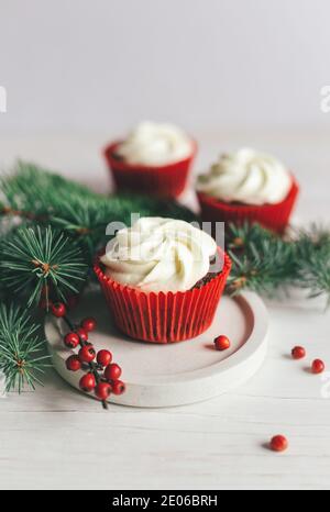 Leckere Cupcakes mit Fichtenzweigen und roten Beeren auf weißem Hintergrund dekoriert. Süßigkeiten für die Feier Weihnachten. Urlaub umweltfreundliche concep Stockfoto