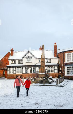 Menschen, die an den alten sächsischen Steinkreuzen in der vorbeigehen Gepflasterter schneebedeckter Marktplatz im Winter bei Sandbach Cheshire England Stockfoto