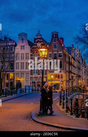 Amsterdam Niederlande bei Sonnenuntergang, historische Kanäle bei Sonnenuntergang. Holländische historische Grachten in Amsterdam, Paar auf Städtereise in Amsterdam, Männer und Frauen am Abend an den Grachten Stockfoto