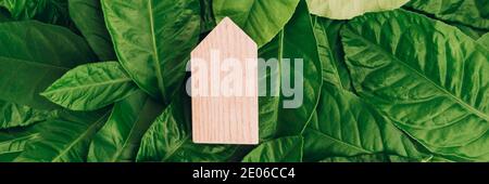 Banner mit Miniatur-Holzhaus auf grünen Blättern. Umweltfreundliches und energieeffizientes Hauskonzept. Nahaufnahme. Stockfoto