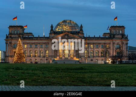 28. Dezember 2020, das Berliner Reichstagsgebäude von Baumeister Paul Wallot am Platz der Republik mit Fahnen und Weihaftertsbaum, beleuchtet am Abend zur blauen Stunde. Vorderseite des Gebäudes mit dem Schriftzug 'dem Deutschen Volk'. Der Reichstag ist Sitz des Deutschen Bundestages mit Plenarsaal. Weltweite Nutzung Stockfoto