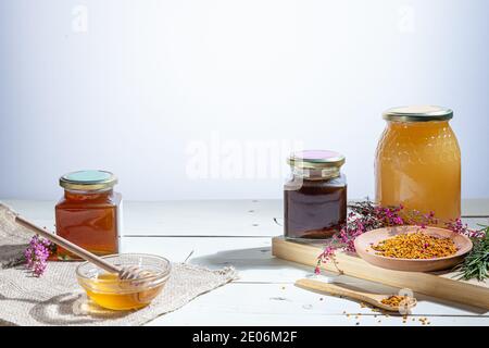 Honiggläser mit Honigstöcken, Blumen und Bienenpollen Weißer Hintergrund aus Holz Stockfoto