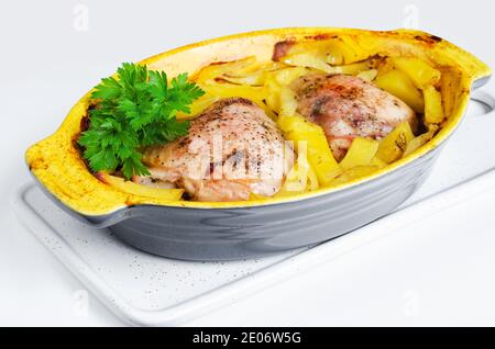 Hähnchen gebacken mit Kartoffeln in einer Auflaufform, ein paar Grüns auf der Oberseite. Weißer Hintergrund, selektiver Fokus Stockfoto