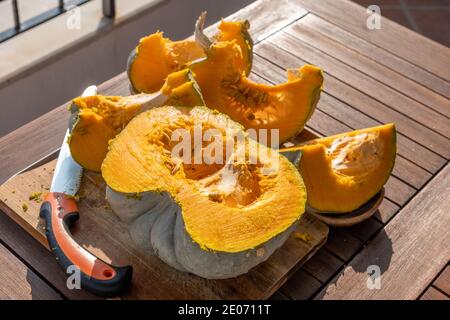 Draufsicht auf einen frisch geschnittenen Kürbis auf einem Holztisch unter Sonnenlicht. Die Frucht wurde vor kurzem mit einer Säge geschnitten. Innen roh und Gemüsesamen Stockfoto