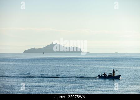 Eine Silhouette eines kleinen Fischerbootes, das vor Inchkeith Island in der Nähe von Kinghorn Harbour, Fife, Schottland segelt. Stockfoto