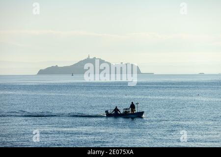 Eine Silhouette eines kleinen Fischerbootes, das vor Inchkeith Island in der Nähe von Kinghorn Harbour, Fife, Schottland segelt. Stockfoto