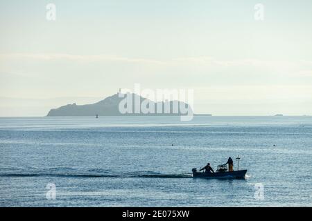 Eine Silhouette eines kleinen Fischerbootes, das vor Inchkeith Island in der Nähe von Kinghorn Harbour, Fife, Schottland segelt. Stockfoto