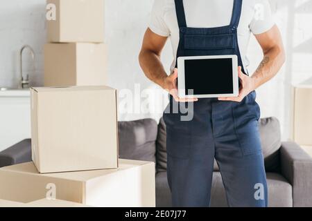 Beschnittene Ansicht von Mover in Uniform halten digitale Tablette mit Leere Leinwand in der Nähe von Boxen in der Wohnung Stockfoto