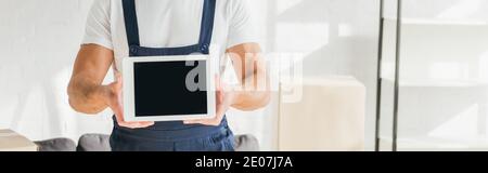 Beschnittene Ansicht von Mover in Uniform halten digitale Tablette mit leeren Bildschirm in der Nähe von Boxen in der Wohnung, Banner Stockfoto