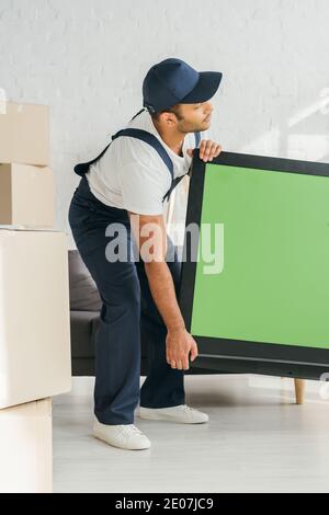 Indian Mover in Uniform trägt Plasma-tv mit grünem Bildschirm In der Wohnung Stockfoto