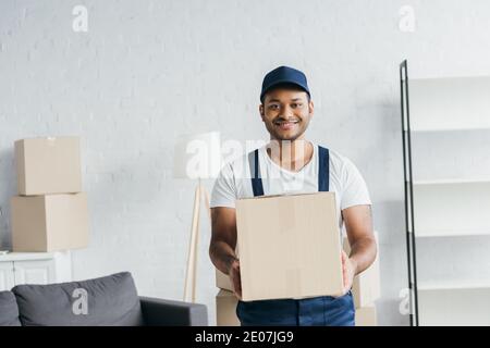 Junge fröhliche indische Kurier in Kappe und einheitliche Holding-Box In der Wohnung Stockfoto