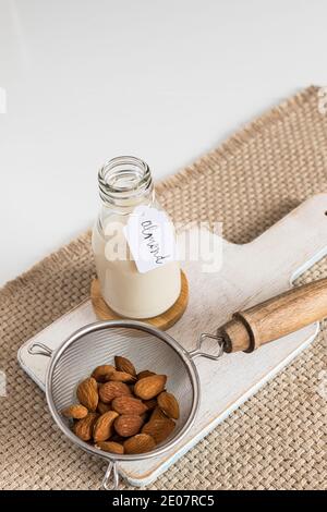 Mandelmilch in einer Flasche neben einem Sieb voller Mandeln auf einem Schneidebrett gekennzeichnet. Vertikale Ansicht. Stockfoto