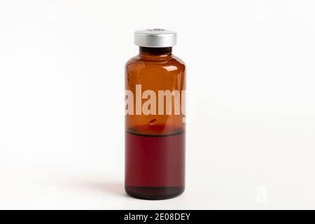 Eine Makroaufnahme mit selektivem Fokus einer bernsteinfarbenen Impfstoffflasche auf einem schlichten weißen Hintergrund. Stockfoto