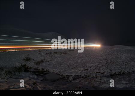 Glencoe, Schottland, Großbritannien. Dezember 2020. Im Bild: Die A82 mit einem einsamen Fahrzeug in der Nacht unter dem abnehmenden Herbstmond gesehen. Der Schnee reflektiert das Licht zurück und verursacht ein dramatisches Nachtbild. Gelbe Schneewarnung an Ort und Stelle, da mehr Schnee mit frostigen Temperaturen über Nacht erwartet wird. Quelle: Colin Fisher/Alamy Live News Stockfoto