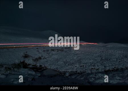 Glencoe, Schottland, Großbritannien. Dezember 2020. Im Bild: Die A82 mit einem einsamen Fahrzeug in der Nacht unter dem abnehmenden Herbstmond gesehen. Der Schnee reflektiert das Licht zurück und verursacht ein dramatisches Nachtbild. Gelbe Schneewarnung an Ort und Stelle, da mehr Schnee mit frostigen Temperaturen über Nacht erwartet wird. Quelle: Colin Fisher/Alamy Live News Stockfoto