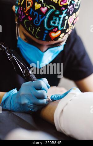 Latin Frau Tattoo Künstler zeigt den Prozess der Tätowierung Mit Farbe und arbeitet in blauen sterilen Handschuhen in Mexiko Stadt Stockfoto