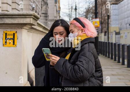 London, Großbritannien. Dezember 2020. Frauen nutzen ein Smartphone der Straße.als die tägliche Covid19-Infektionsrate in London auf Rekordhoch trifft, setzt die Regierung ihre Hoffnungen auf die Oxford/AstraZeneca Jab. Kredit: SOPA Images Limited/Alamy Live Nachrichten Stockfoto