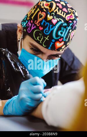 Latin Frau Tattoo Künstler zeigt den Prozess der Tätowierung Mit Farbe und arbeitet in blauen sterilen Handschuhen in Mexiko Stadt Stockfoto