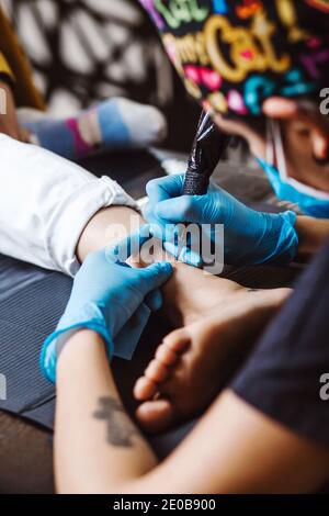 Latin Frau Tattoo Künstler zeigt den Prozess der Tätowierung Mit Farbe und arbeitet in blauen sterilen Handschuhen in Mexiko Stadt Stockfoto