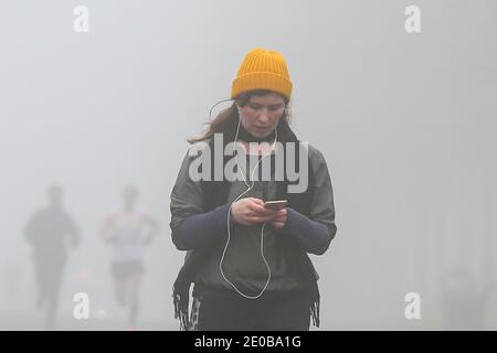 London, Großbritannien. Dezember 2020. Eine Frau benutzt ihr Handy in einem Park während eines dichten Nebels in London. Kredit: SOPA Images Limited/Alamy Live Nachrichten Stockfoto