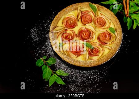 Schöne hausgemachte Apfelkuchen auf schwarzem Hintergrund mit grünen Blättern und Zimtstangen. Stockfoto