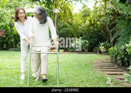 Eine alte ältere asiatische Frau benutzt einen Spaziergänger und läuft im Hinterhof mit ihrer Tochter. Konzept der glücklichen Ruhestand mit Betreuung von einem Betreuer und Sa Stockfoto