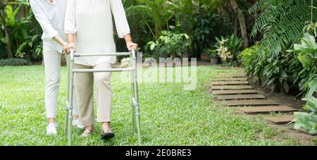 Eine alte ältere asiatische Frau benutzt einen Spaziergänger und läuft im Hinterhof mit ihrer Tochter. Konzept der glücklichen Ruhestand mit Betreuung von einem Betreuer und Sa Stockfoto