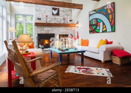 Old Canadiana hölzerner Schaukelstuhl, Folk Art Couchtisch, weißes Polstersofa mit bunten Velours-Kissen im Familienzimmer Stockfoto