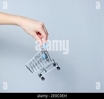 Weibliche Hand hält einen Mini-Einkaufswagen auf grauem Hintergrund. Einkaufskonzept Stockfoto