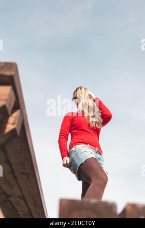 Kaukasische blonde Frau mit rotem Pullover und Sonnenbrille posiert im Freien. Stockfoto