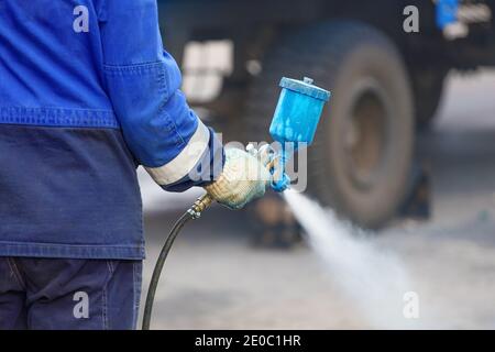 Spritzpistole in der Hand. Ein Arbeiter in Overalls und einem Handschuh hält einen Sprühkompressor zum Malen in der Hand. Stockfoto