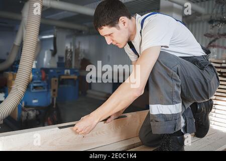 Ein junger Mann arbeitet in einer Schreinerei. Ein Mitarbeiter mißt Holz mit einem Lineal Stockfoto