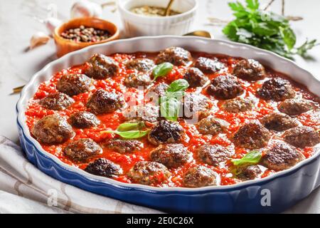 Italienische Fleischbällchen aus gehacktem Schweinefleisch mit Hackfleisch in einer klassischen Marinara-Sauce mit frischem Basilikum auf der Oberseite, Knoblauch, Pfefferkörner auf einem Lig Stockfoto